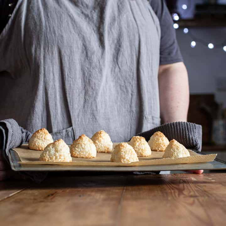 woman in grey holding baking tray of coconut pyramids in a rustic wooden kitchen