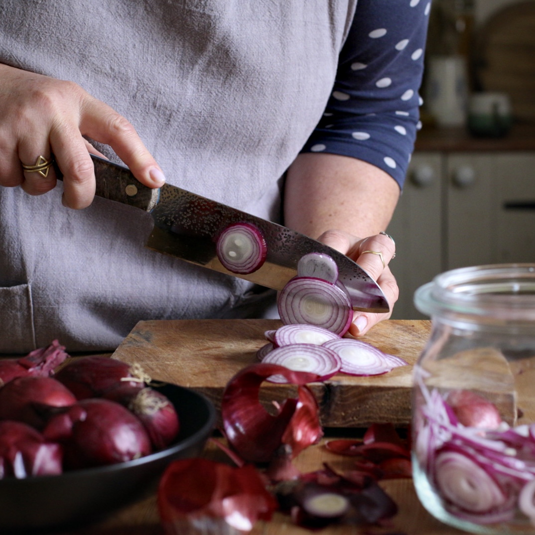 Womans hands thinly slicing red onions on a wooden chopping board