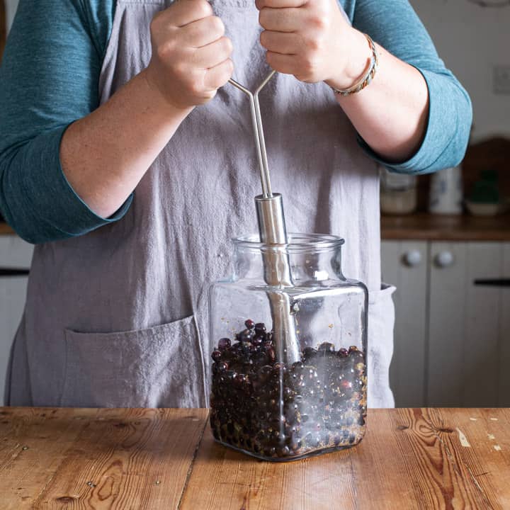 woman in grey mashing a glass jar of blackcurrants