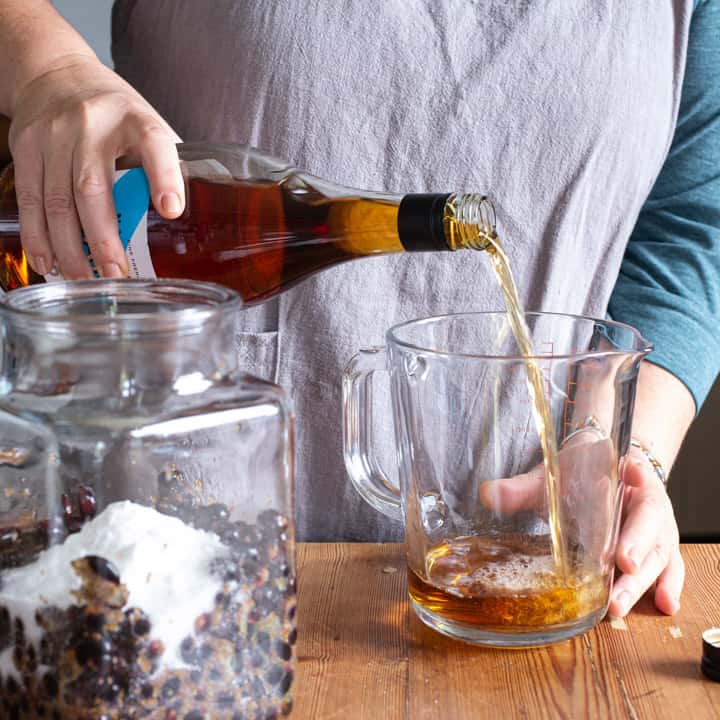 woman pouring brandy from a glass bottle into a glass measuring jug