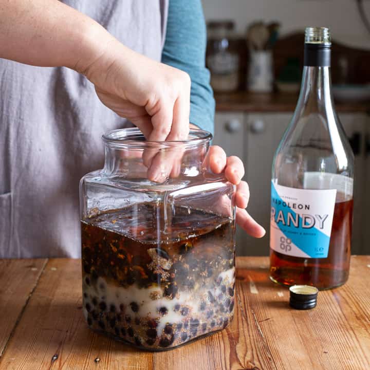 woman stirring a jar of blackcurrants, sugar and brandy to make traditional creme de cassis liqueur 