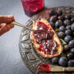 a spoon of wild sloe and blackberry jam held over a piece of toast and damsons on a pewter plate