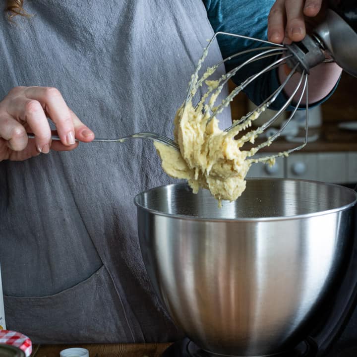 womans hands scraping cake batter from an electric mixer whisk into a mixing bowl