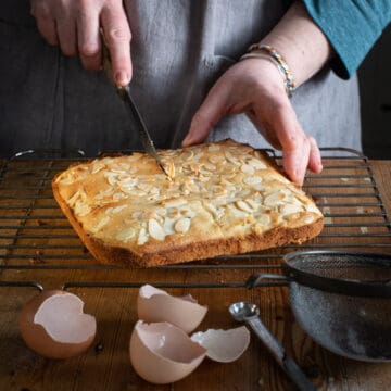womans hands cutting a homemade tray bake cake on a wooden kitchen counter