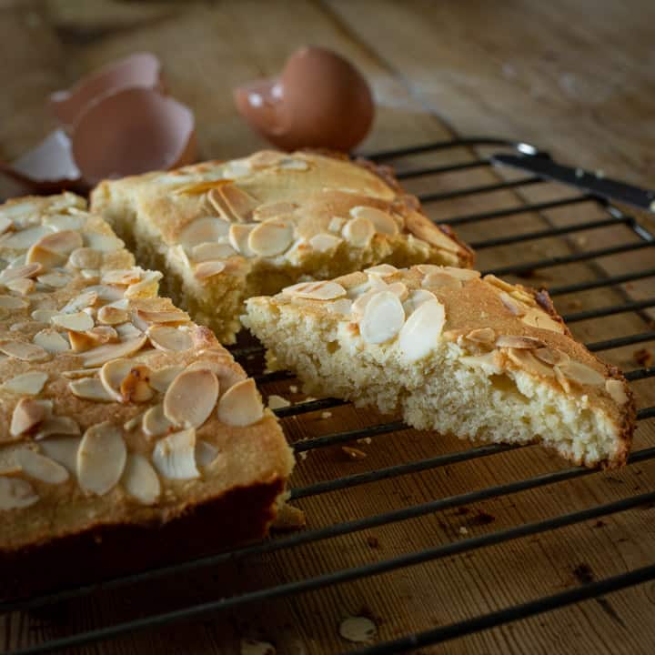 wooden kitchen counter with wire cooling tray and a golden brown almond cake cut into triangles