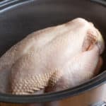 black slow cooker pot with raw whole chicken inside