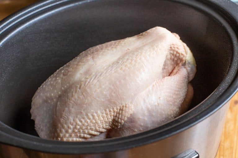 black slow cooker pot with raw whole chicken inside