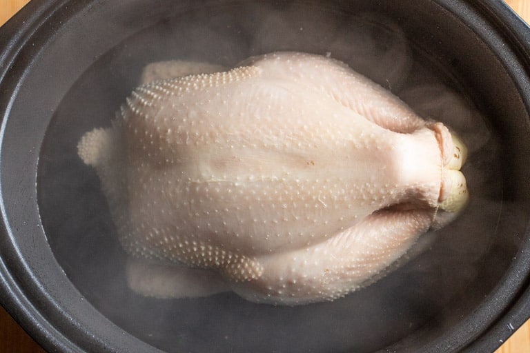 black slow cooker pot with raw whole chicken inside