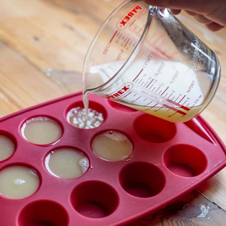 glass just pouring chicken stock into red silicone muffin tray for freezing