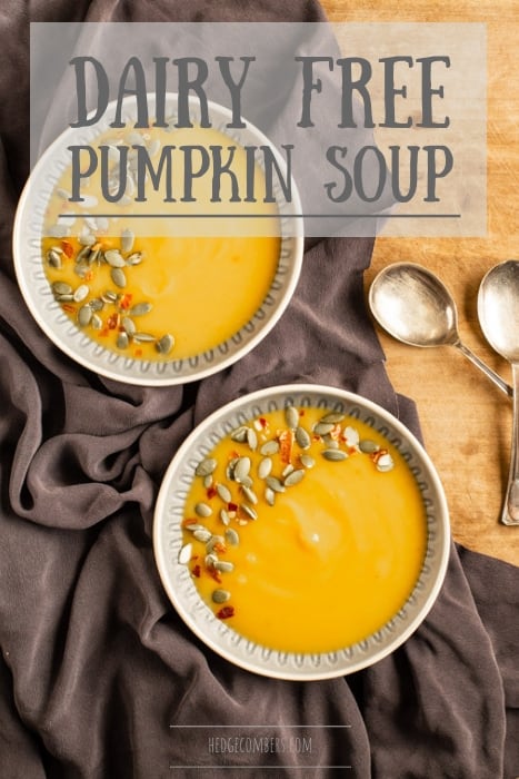 wooden background with two bowl of dairy free pumpkin soup sprinkled with pumpkin seeds and chilli flakes