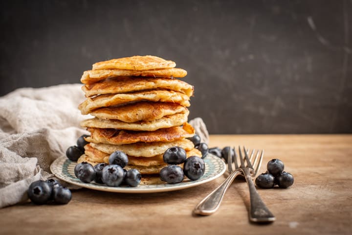 black background with stack of eggless pancakes with blueberries 