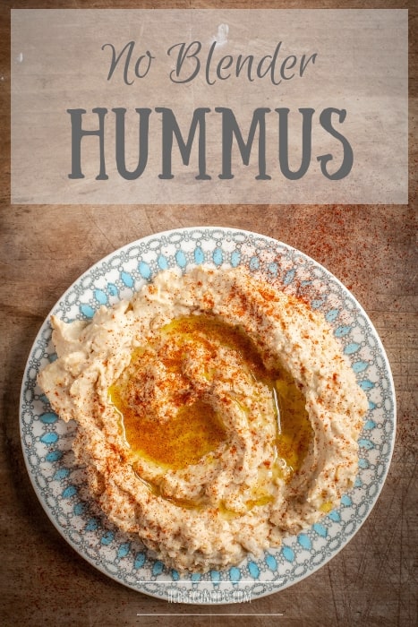 wooden bakground with pretty plate filled with homemade hummus drizzled with olive oil and smoked paprika