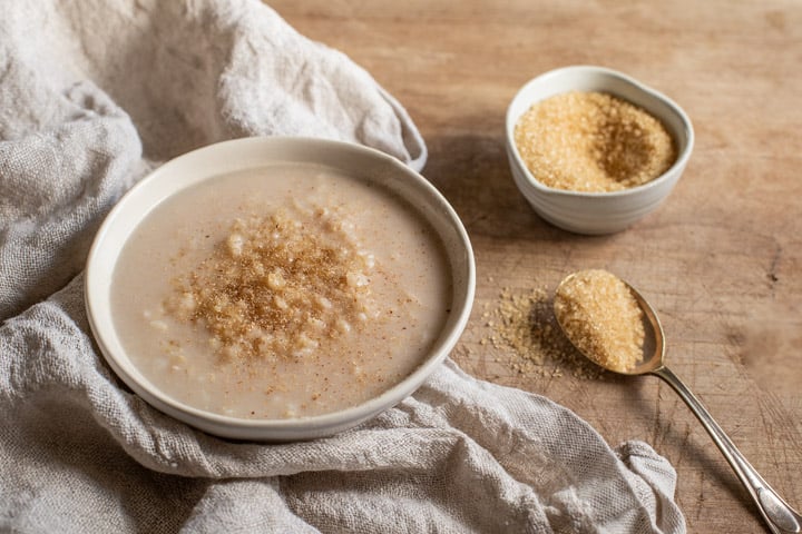 rustic white bowl filled with easy stovetop rice pudding and sprinkled with brown sugar and cinnamon