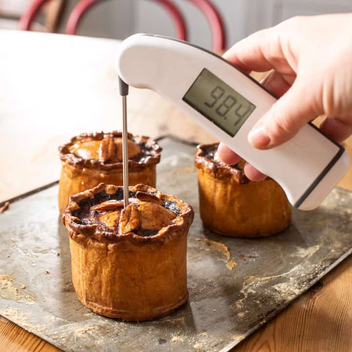 3 handmade British pork pies being tasted for their internal temperature with a white digital thermometer