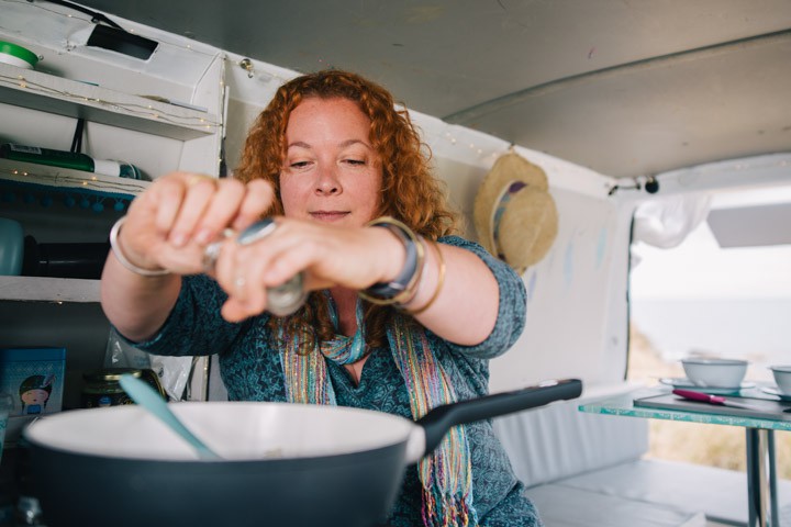 Jane Sarchet grinding a pepper mill over a saute pan in her VW campervan