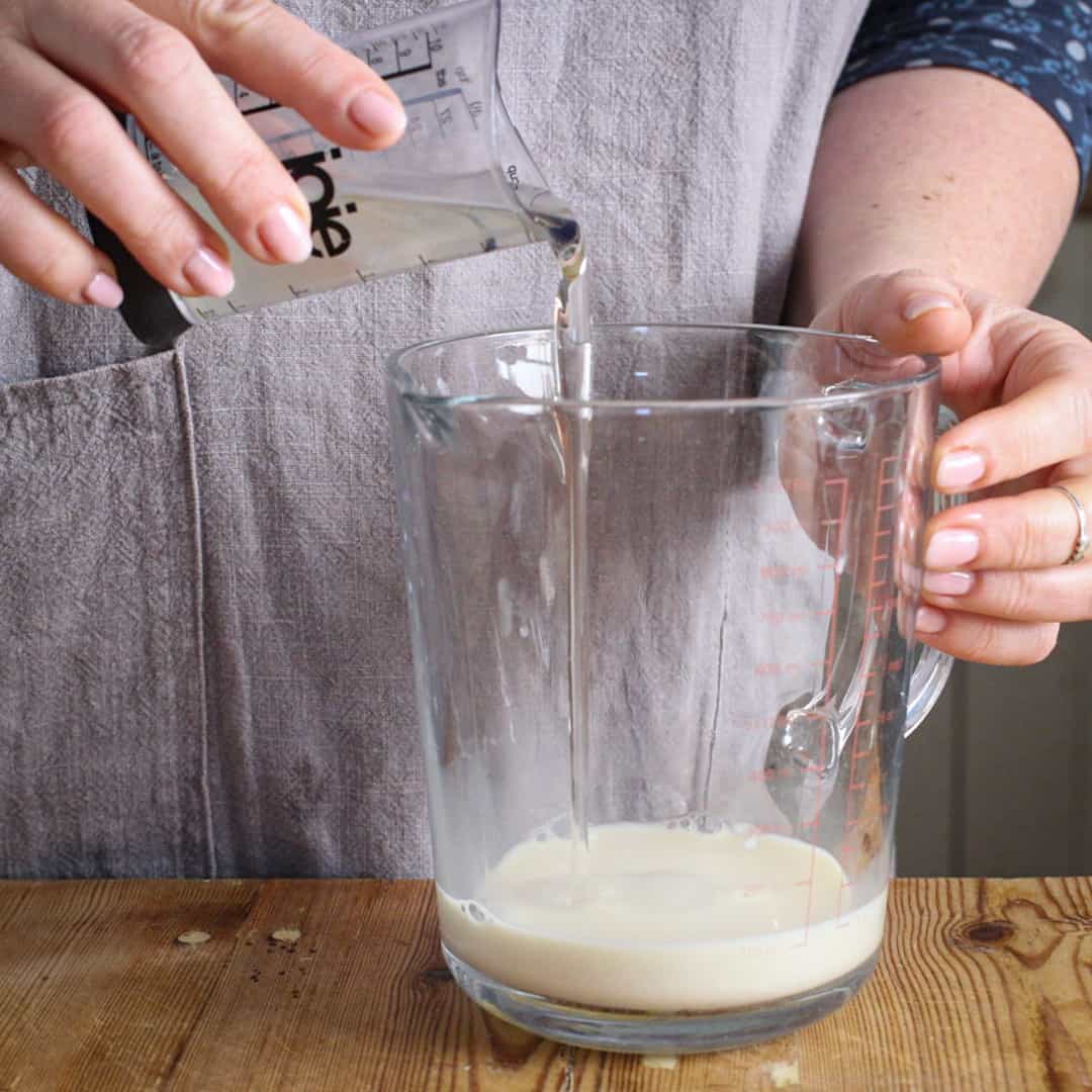 Womans hands pouring oil from a small measuring cup into a glass jug