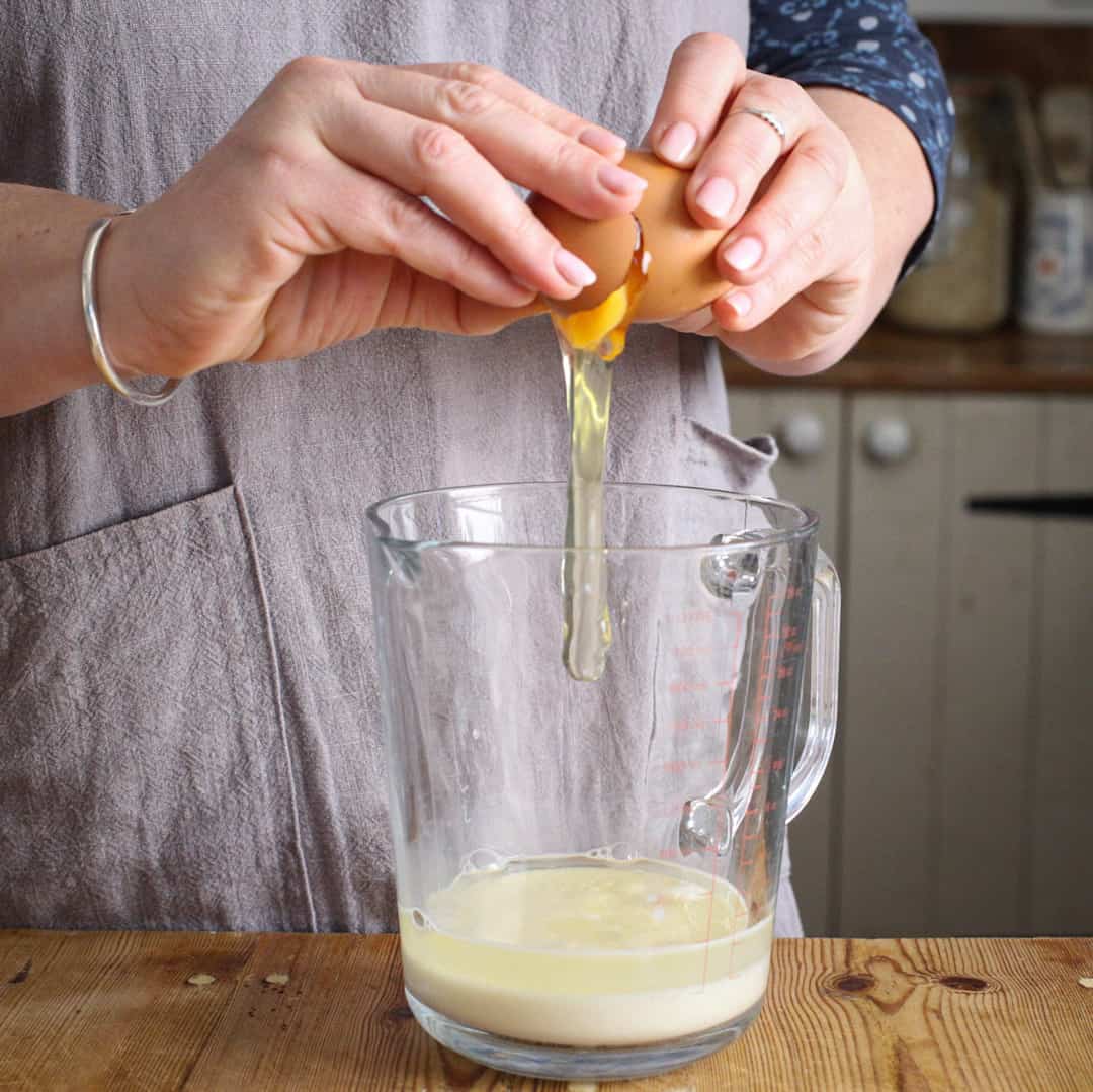 Woman cracking an egg into a glass just of milk to make muffins