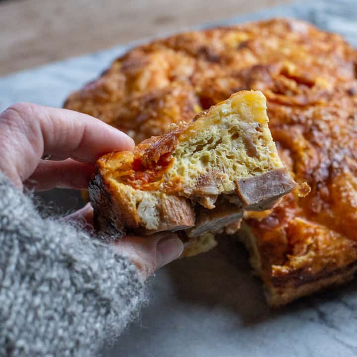 ladies hand holding a piece of full English breakfast frittata