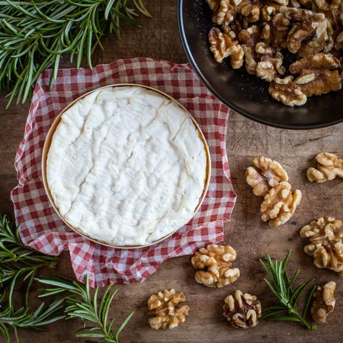 wooden board scatted with walnuts sprigs of rosemary and a round white Camembert cheese