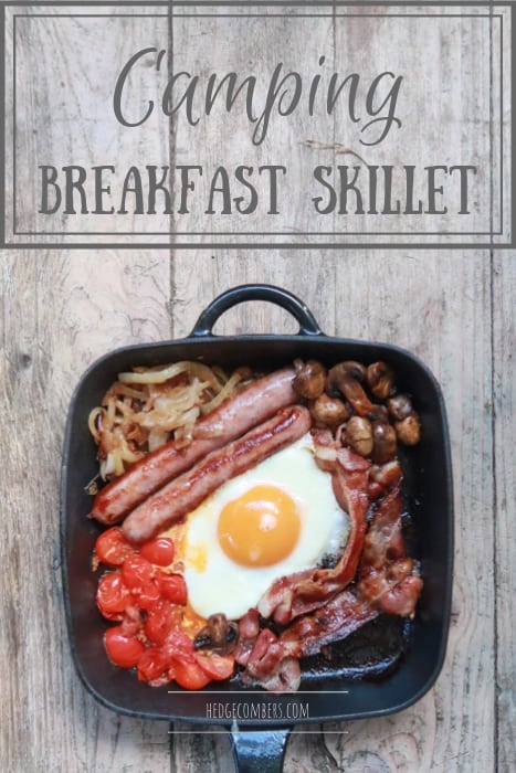 wooden background with cast iron breakfast skillet filled with breakfast foods like sausages, bacon, eggs, mushrooms etc