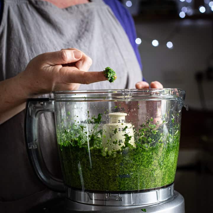 woman in a kitchen taking a small amount of homemade pesto on her finger to taste