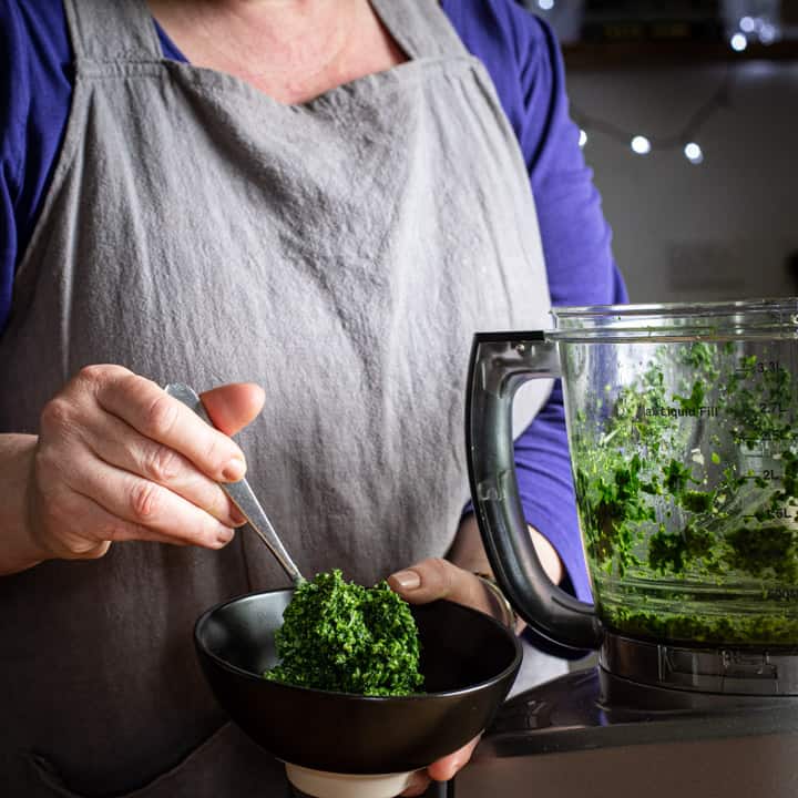 woman spooning wild garlic pesto into a small black bowl from a food processor