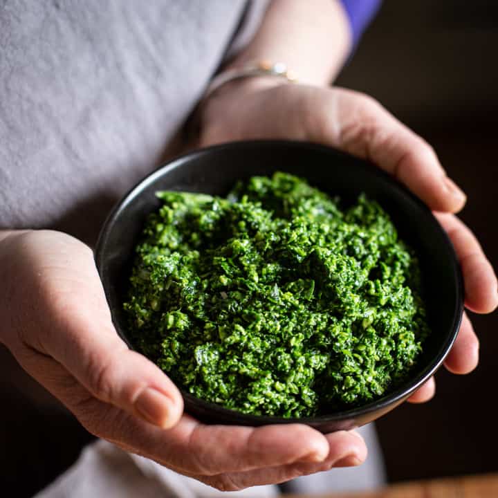 womans hands holding a small black bowl of wild garlic pesto