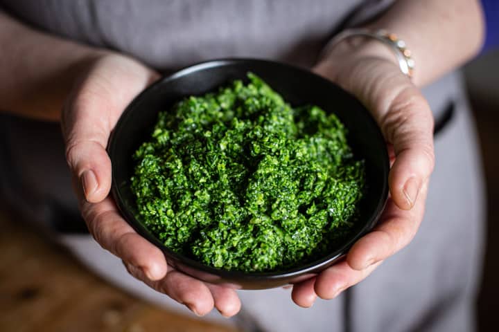 woman in grey holding a black bowl or bright green homemade ramson pesto