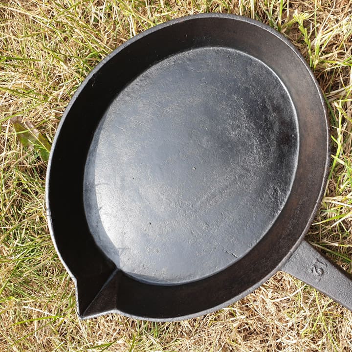 Shiny, well seasoned cast iron skillet sat on the grass