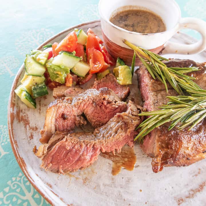 white plate on blue table with a juicy sliced sirloin steak and salad