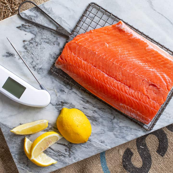 Piece of salmon prepared for smoking on marble chopping board with fresh lemon