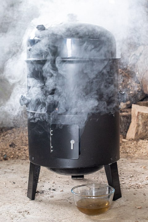 A black tower smoker surrounded by white smoke, hot smoking wild salmon