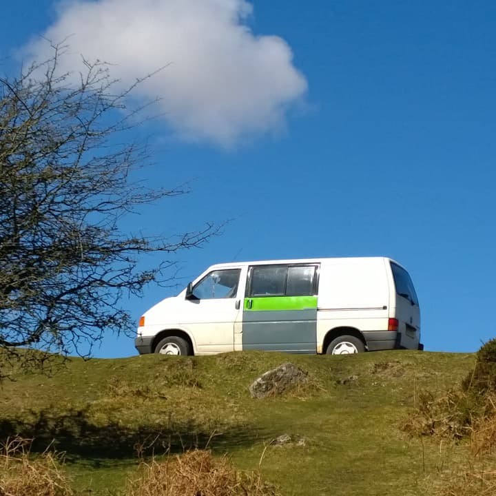 scruffy old VW T4 van with white, green and grey bodywork against a blue sky