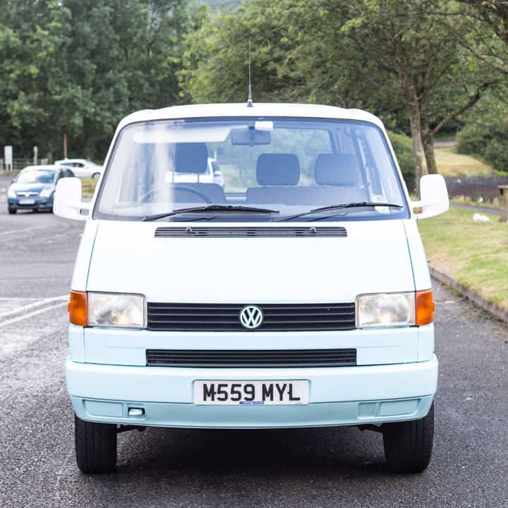 head on shot of a pale blue and white VW T4 campervan parked in a car park