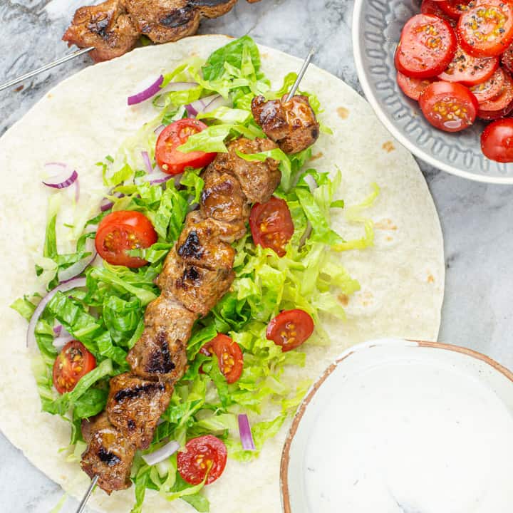 marble board with bbq lamb kebabs, flatbread and fresh salads