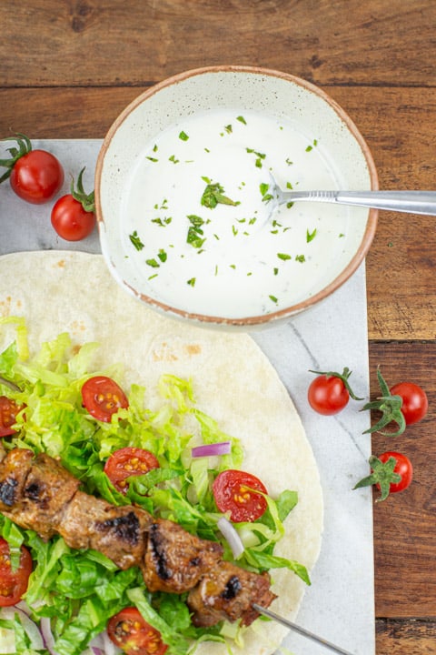 marble board with bbq lamb kebabs, flatbread and fresh salads