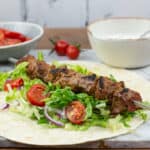 marble board with bbq lamb kebabs, flatbread and fresh salads