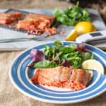 blue and white plate with a piece of hot smoke salmon, salad leaves and lemon wedge