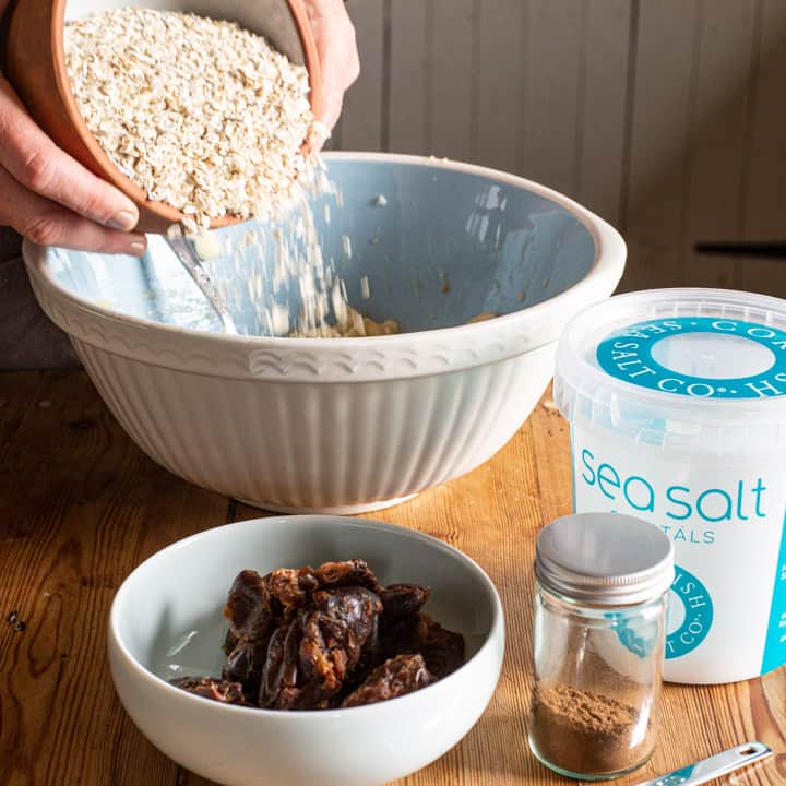 woman hands tipping oats from a small terracotta bowl into a large mixing bowl