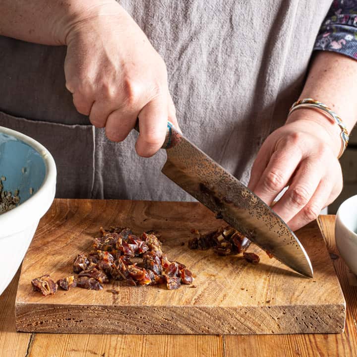 woman in grey chopping dates on a wooden board