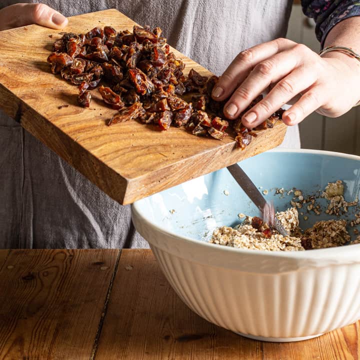 woman in grey tipping chopped dates from a wooden board into a blue and white mixing bowl