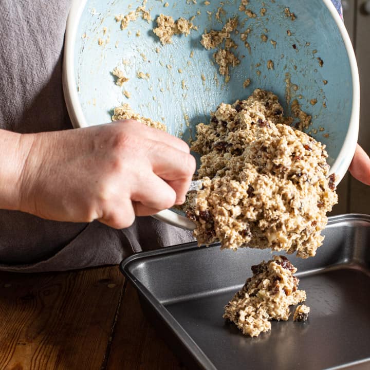 woman tipping fruity oat mixture into a baking tin to make flapjacks