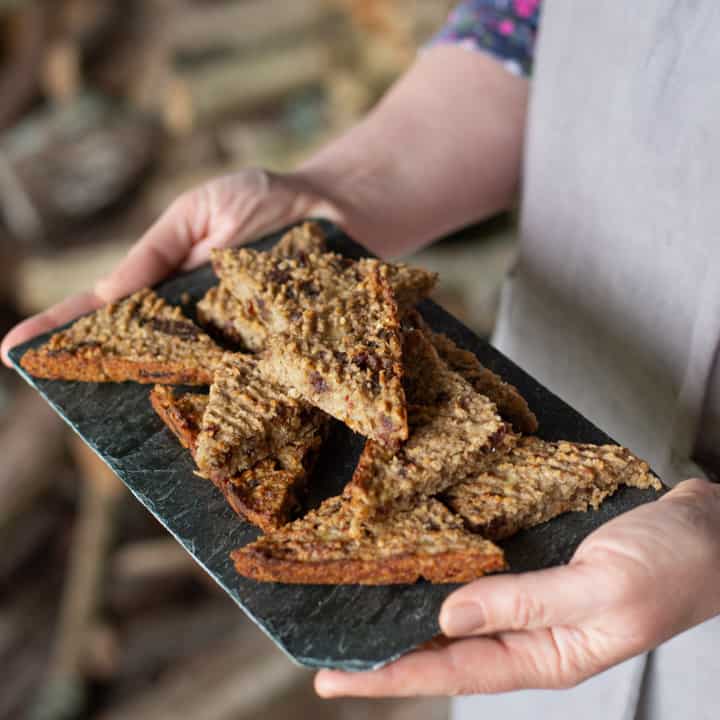 woman in grey holding a piece of slate stacked with triangles of flapjack oat slices