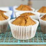 pumpkin spice muffins in white paper wrapper on a pale blue wire cooling rack