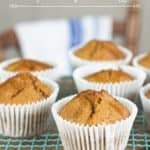 pumpkin spice muffins in white paper wrapper on a pale blue wire cooling rack