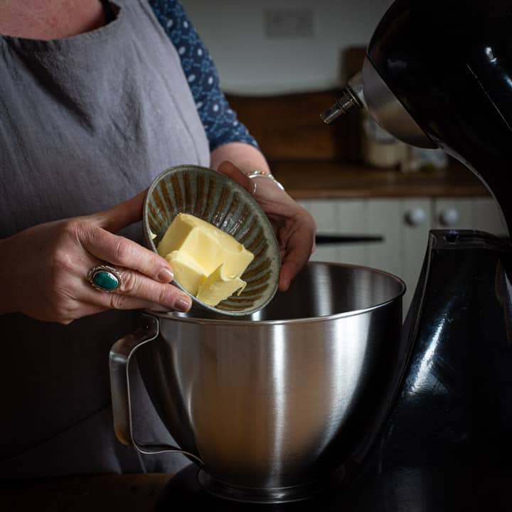 womans hands tipping block of butter from small brown bowl into a large silver mixing bowl