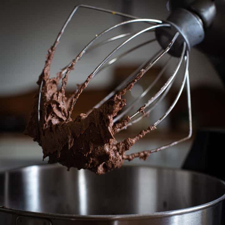 close up of a mixer whisk full of chocolate buttercream 