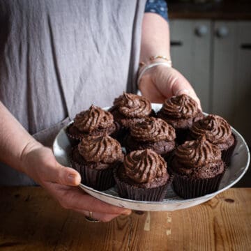 woman in grey holding a tray of chocolate muffins topped with chocolate orange buttercream