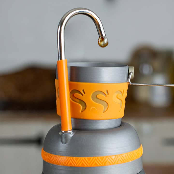 grey and orange stove top chub coffee maker blowing a bubble of coffee into a small cup