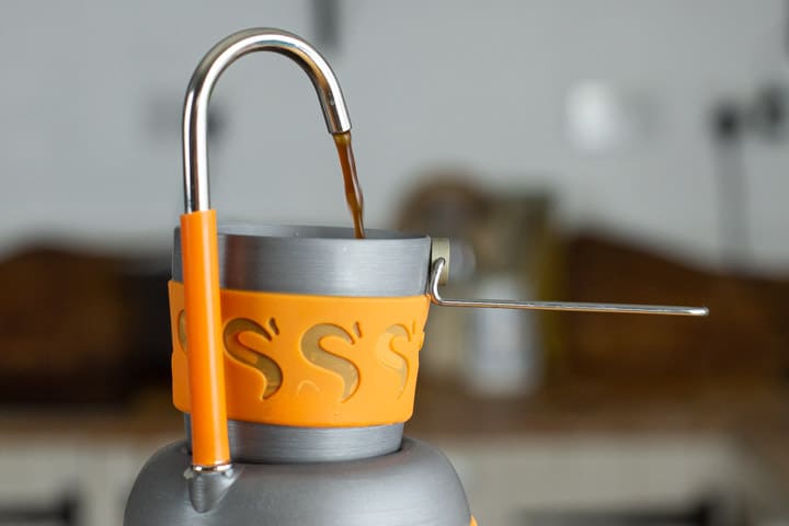 grey and orange stove top chub coffee maker pouring espresso coffee into a small cup